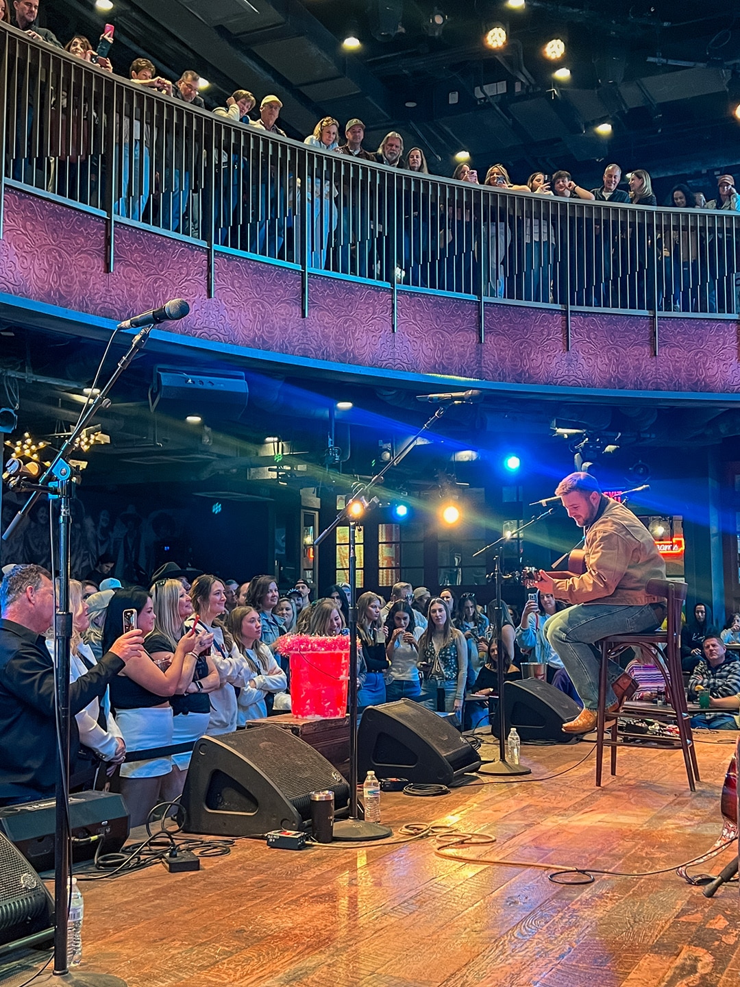 A performer on stage with crowds watching from the mezzanine and the ground floor